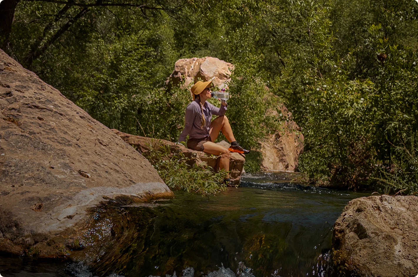 Hiker resting on a rock beside a creek pool in Aravaipa Canyon