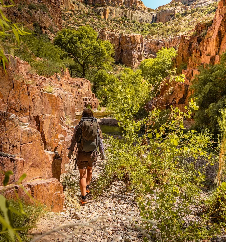 Backpacker hiking a rocky trail between red canyon walls in Aravaipa