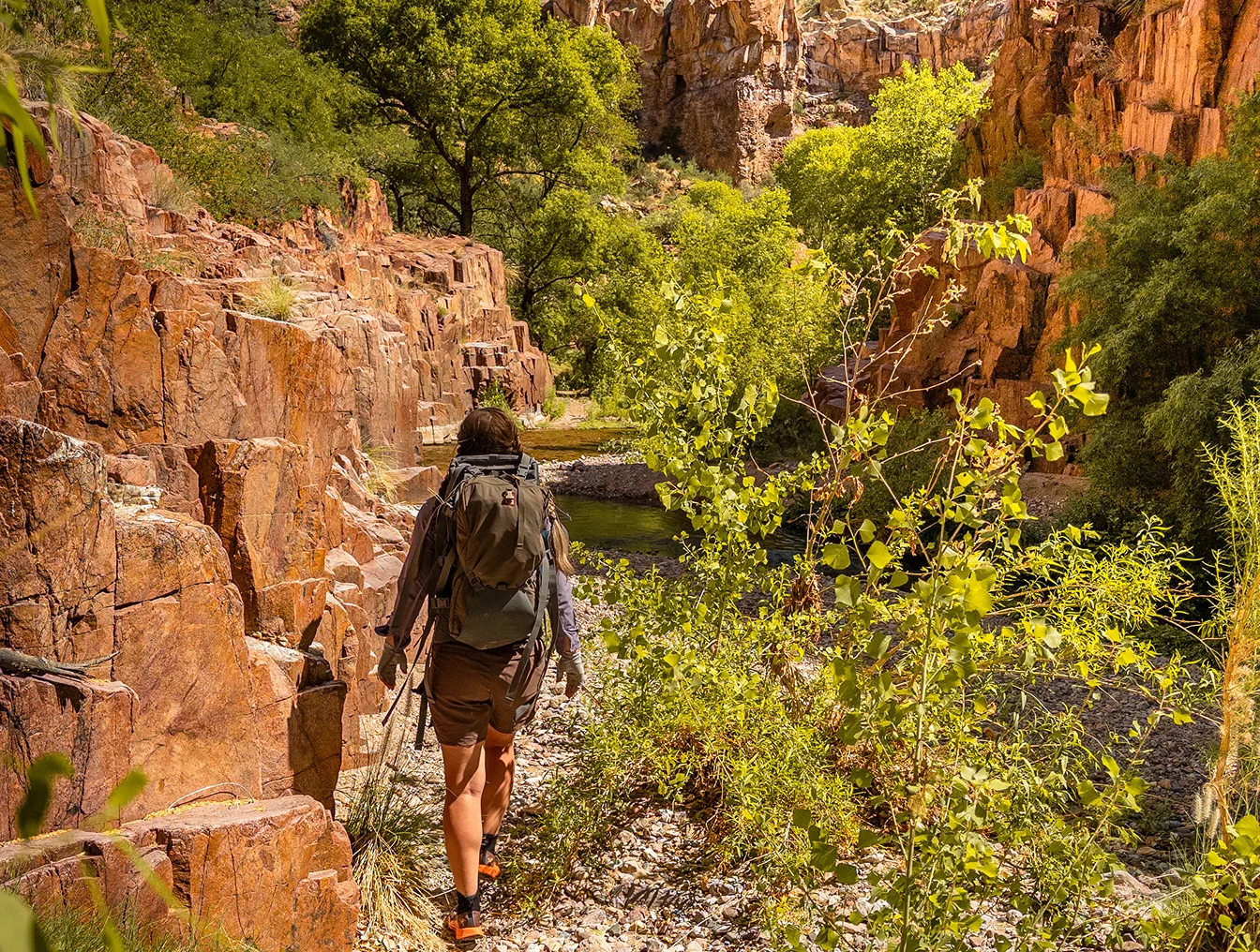 Backpacker hiking a rocky trail between red canyon walls in Aravaipa