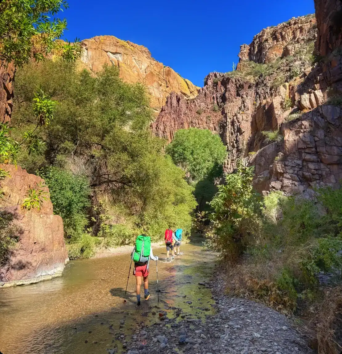 Group of backpackers hiking along Aravaipa Creek between red canyon walls