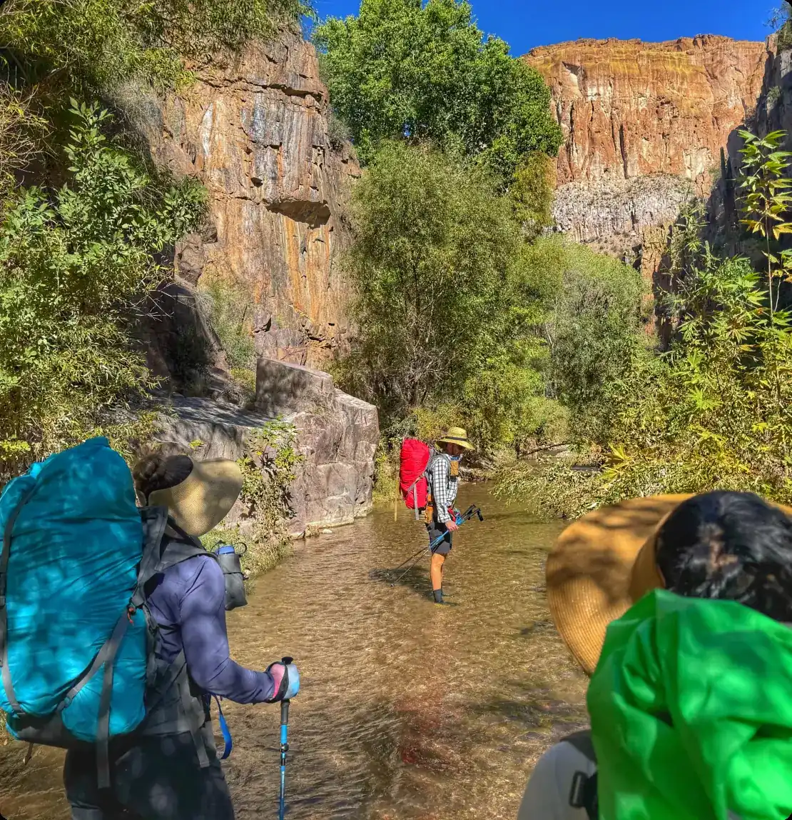 Group of hikers with backpacks wading through Aravaipa Creek