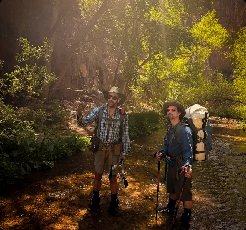 Two hikers with backpacks in a shaded Aravaipa Canyon creek